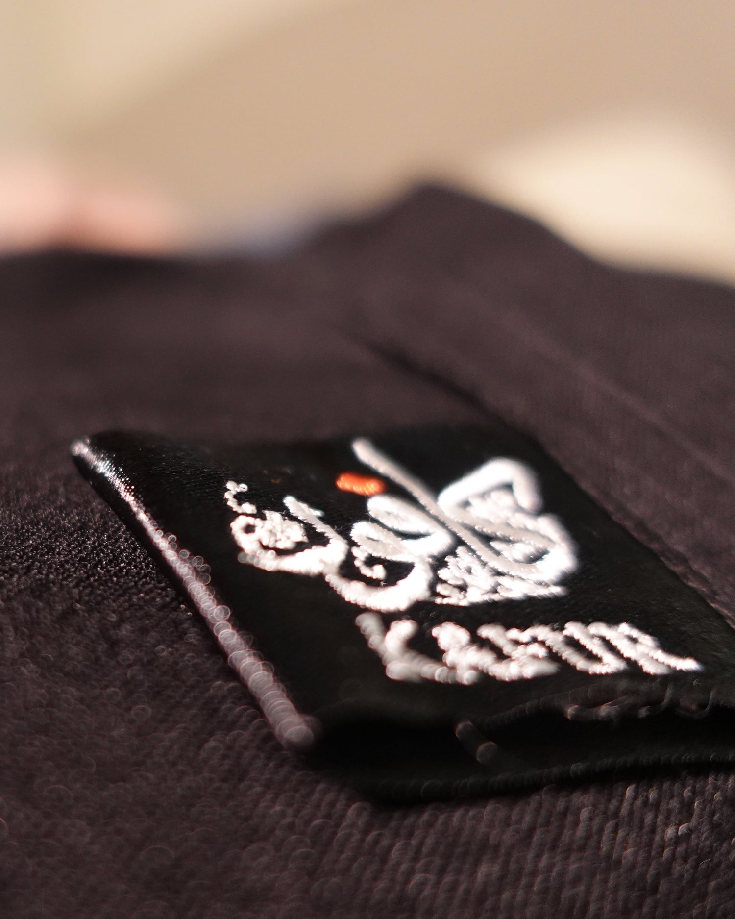 Close-up of a black fabric garment with a sewn-on brand patch reading 'KAFUR' and featuring a butterfly graphic.